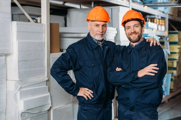 Travailleurs masculins dans les casques étreignant et posant dans l'entrepôt — Photo de stock