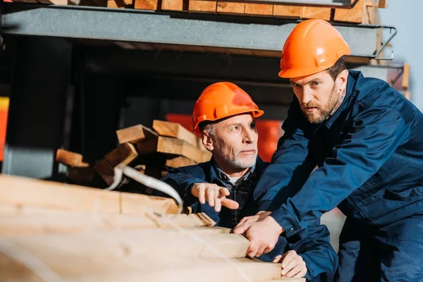 Two builders in helmets working with wooden planks outside on construction — Stock Photo