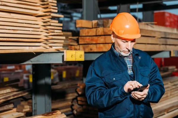 Senior builder in helmet using smartphone outside on construction — Stock Photo