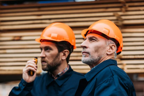 Dos constructores en cascos trabajando con walkie talkie fuera en la construcción - foto de stock