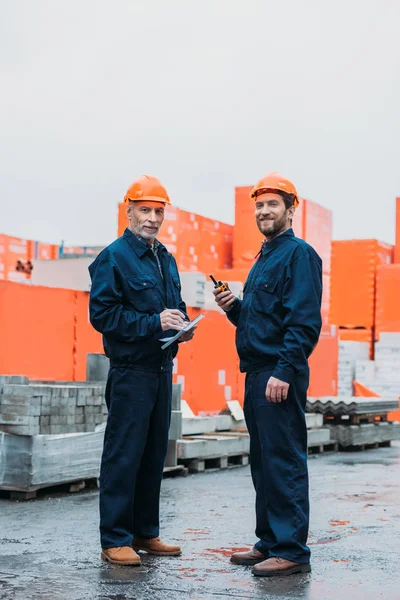 Bauarbeiter in Helmen arbeiten mit Walkie Talkie und Notizblock draußen auf der Baustelle — Stockfoto