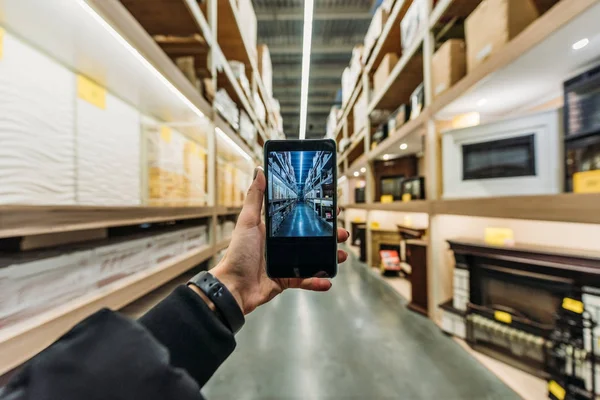 Ausgeschnittene Ansicht der Person, die ein Foto der Lagerhalle auf dem Smartphone macht, Kameraperspektive — Stockfoto