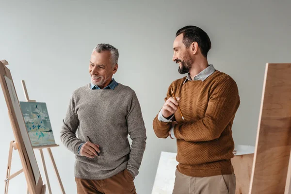 Des artistes seniors masculins souriants se tenant ensemble dans un studio d'art — Photo de stock
