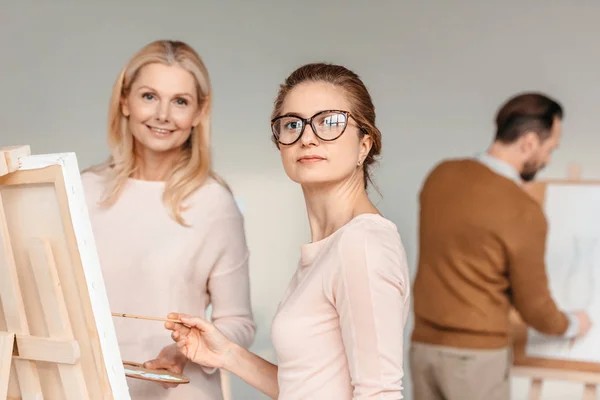 Belles femmes d'âge moyen regardant la caméra tout en peignant ensemble à la classe d'art — Photo de stock