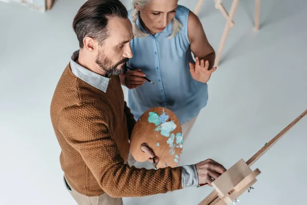 High angle view of mature man holding palette and painting while senior woman standing with pencil near by — Stock Photo