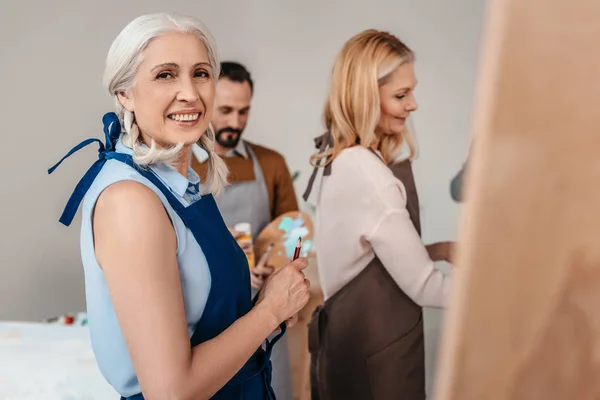 Красивая пожилая женщина улыбается перед камерой во время художественного класса для взрослых — стоковое фото