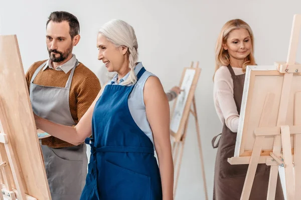 Mature students in aprons painting on easels during art class for adults — Stock Photo