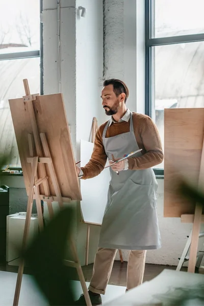 Enfoque selectivo de la pintura masculina madura en caballete en el estudio de arte - foto de stock