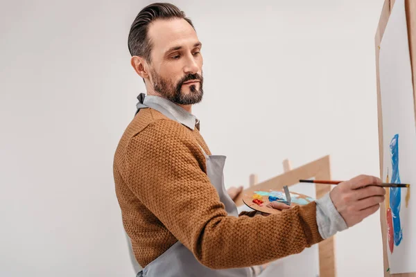 Mature male artist holding palette and painting in art studio — Stock Photo