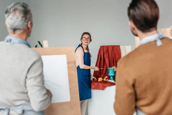 Visão traseira de artistas masculinos olhando para a mulher segurando ferramentas de arte para a vida morta no estúdio de arte — Fotografia de Stock