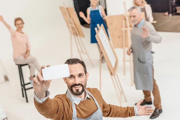 Uomo maturo con smartphone scattare selfie con studenti adulti a lezione d'arte — Foto stock