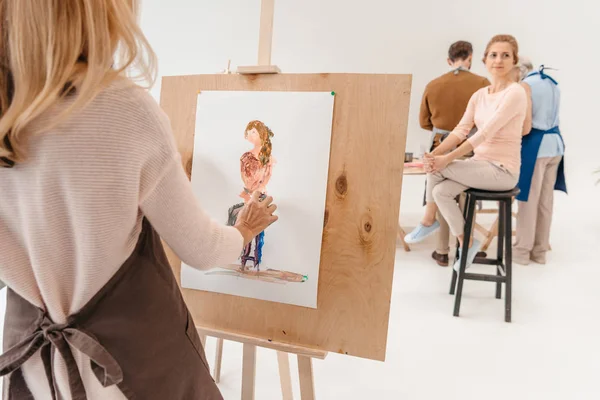 Cropped shot of woman painting on easel while model sitting on chair in art studio — Stock Photo