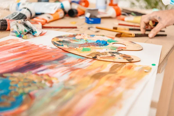 Abgeschnittene Aufnahme menschlicher Hand und Palette mit Farben auf dem Tisch — Stockfoto