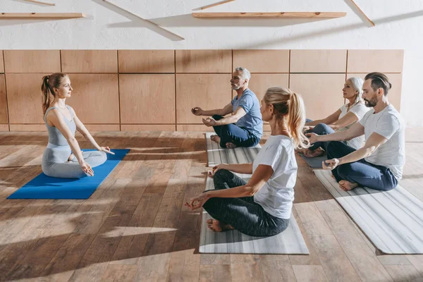 Grupo de personas mayores practicando yoga con instructor en postura de loto en esteras en estudio - foto de stock
