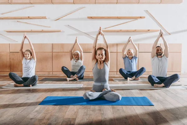 Grupo de personas mayores practicando yoga con instructor en postura de loto en esteras en estudio - foto de stock