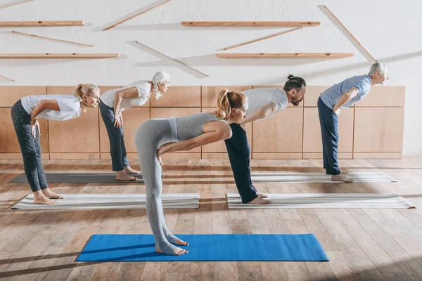 Grupo de personas mayores practicando yoga con instructor en esteras en estudio - foto de stock