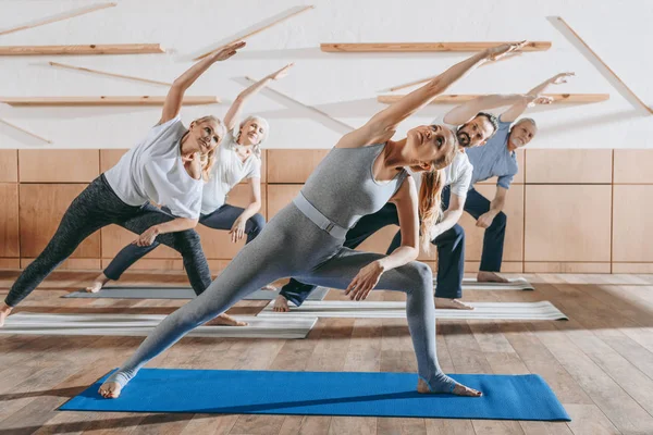 Группа пожилых людей, практикующих йогу и растяжку с инструктором на ковриках в студии — стоковое фото