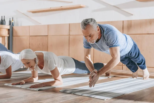 Groupe de personnes âgées faisant planche sur tapis de yoga en studio — Photo de stock