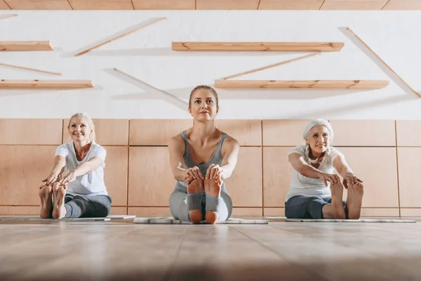 Grupo de mujeres practicando yoga y estirándose sobre esteras en estudio - foto de stock