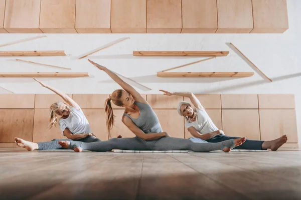 Grupo de mujeres que se estiran y practican yoga sobre esterillas en estudio - foto de stock