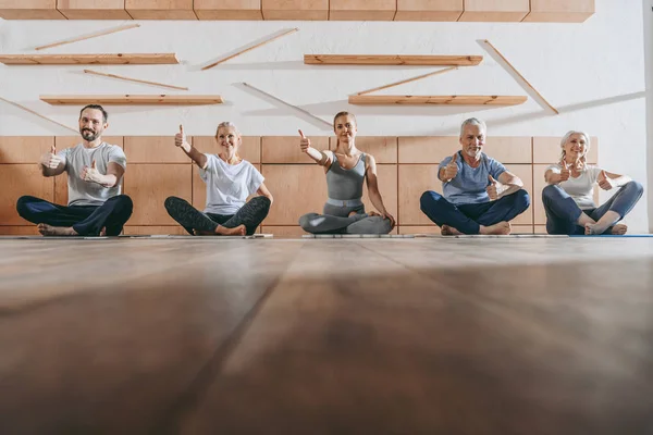 Grupo de personas mayores con pulgares en el estudio de yoga - foto de stock