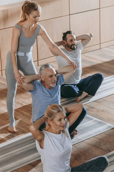Instructora femenina capacitando a personas mayores sentadas en colchonetas de yoga en gimnasio - foto de stock