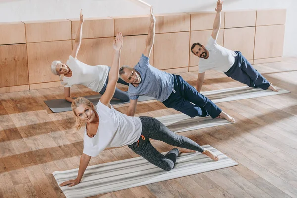 Grupo de personas mayores con instructor haciendo ejercicio sobre esterillas de yoga en el gimnasio - foto de stock