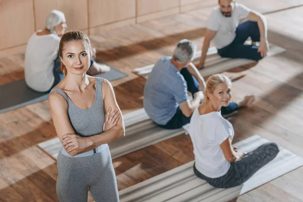 Vista de ángulo alto del instructor femenino mirando la cámara mientras las personas mayores hacen ejercicio en las esteras de yoga - foto de stock