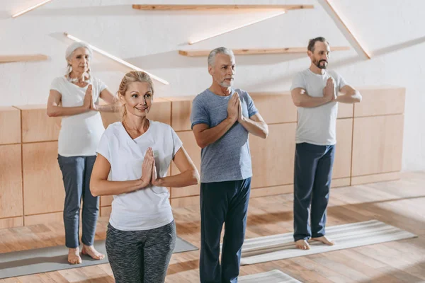 Grupo sênior de pessoas com instrutor praticando ioga na aula de treinamento — Fotografia de Stock