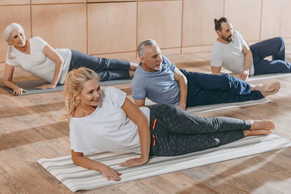 Sonriendo personas mayores entrenando en colchonetas de yoga en clase de entrenamiento - foto de stock