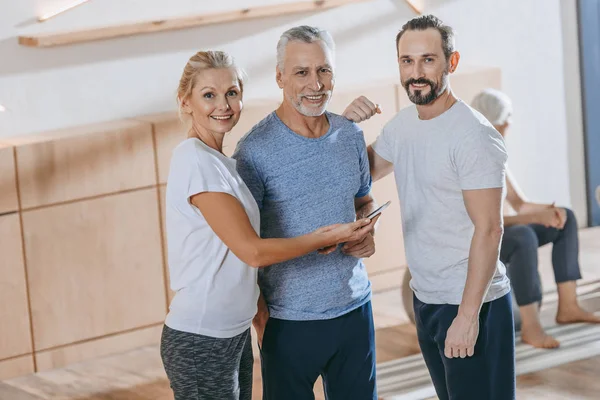 Senior people using smartphone and smiling at camera in fitness studio — Stock Photo