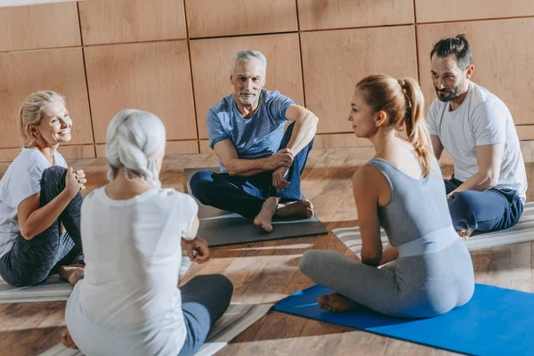 Personas mayores sonrientes con instructor sentado en colchonetas de yoga en la clase de formación - foto de stock
