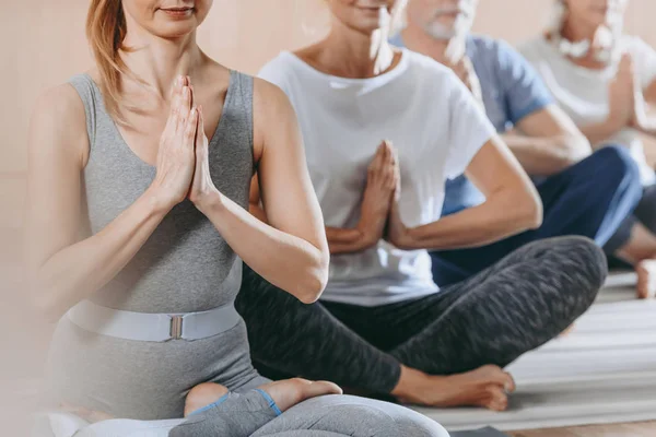 Cropped shot of senior people with instructor sitting in lotus position on yoga mats — Stock Photo