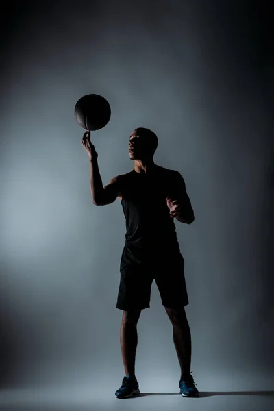 Sportsman afroamericano che gira palla da basket al dito nella stanza buia — Foto stock