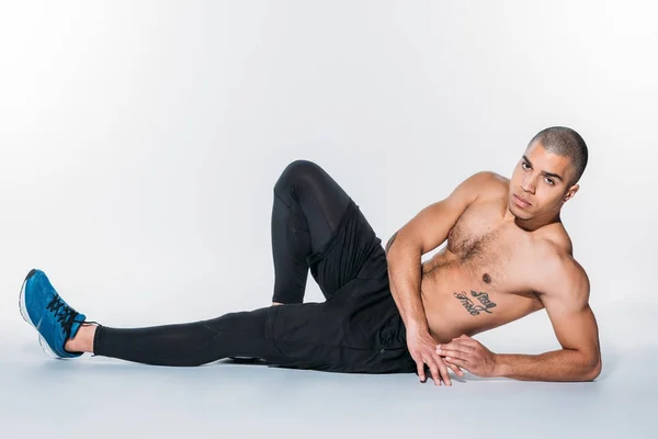 Shirtless tattooed african american sportsman lying on floor and looking at camera — Stock Photo