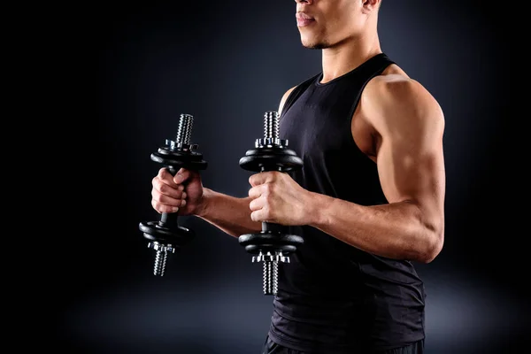 Cropped shot of african american sportsman working out with dumbbells on black — Stock Photo