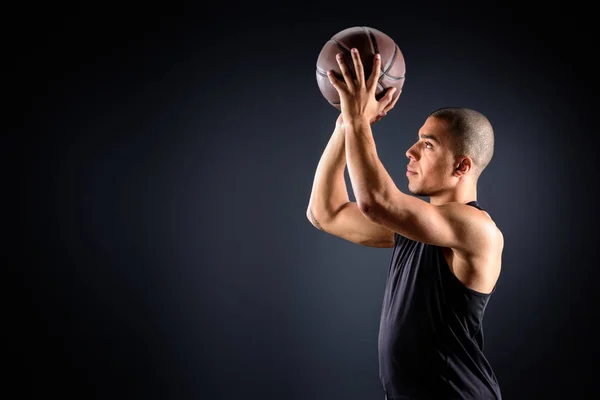 Vista lateral del jugador de baloncesto afroamericano lanzando pelota sobre negro - foto de stock