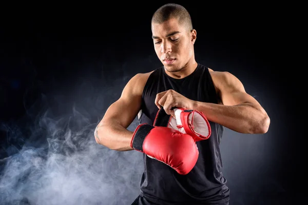 Young african american boxer putting on gloves on black — Stock Photo