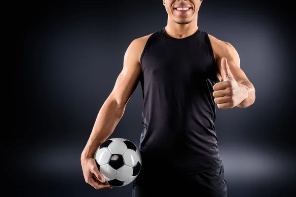 Handsome african american soccer player with ball showing thumb up on black — Stock Photo