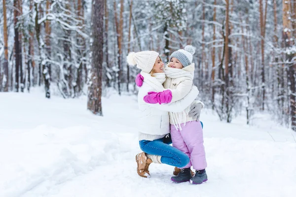 Sorrindo filha e mãe abraçando uns aos outros na floresta de inverno — Fotografia de Stock