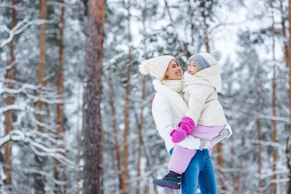 Vue latérale de la mère tenant sa petite fille dans les mains dans la forêt d'hiver — Photo de stock