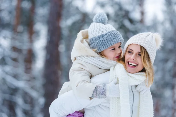 Portrait of cheerful mother and little kid piggybacking together in winter park — Stock Photo