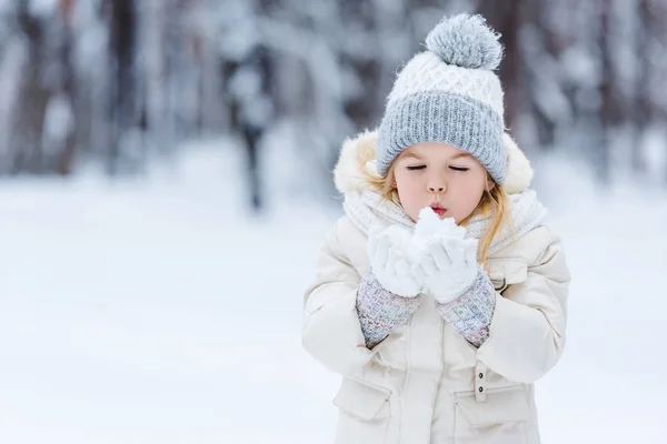 Retrato de adorable niño soplando en bola de nieve en las manos en el parque de invierno - foto de stock
