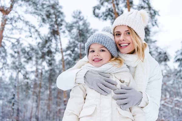 Портрет улыбающейся матери, обнимающей дочь, стоя в зимнем парке — стоковое фото