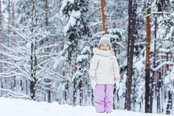 Веселый ребенок смотрит в камеру, стоя в зимнем лесу — стоковое фото
