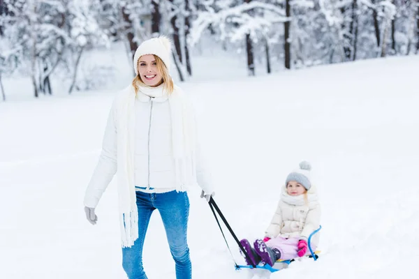 Молода мати і маленька дівчинка катаються в зимовому лісі разом — стокове фото