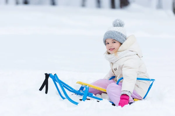 Selective focus of smiling kid sitting on sledge in park — Stock Photo