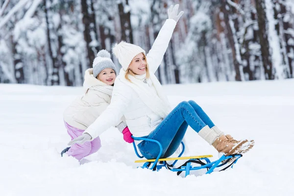 Happy daughter and mother sledging together in winter park — Stock Photo