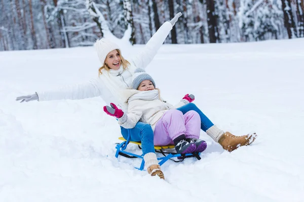 Happy daughter and mother sledging together in winter park — Stock Photo