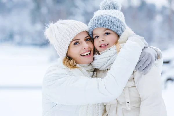 Belle mère heureuse et fille étreignant et souriant à la caméra dans le parc d'hiver — Photo de stock